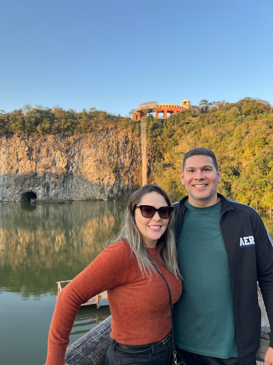 Eduardo Carlota ao lado da esposa, Dra. Sarah Carlota, em um mirante à beira de um lago no litoral.