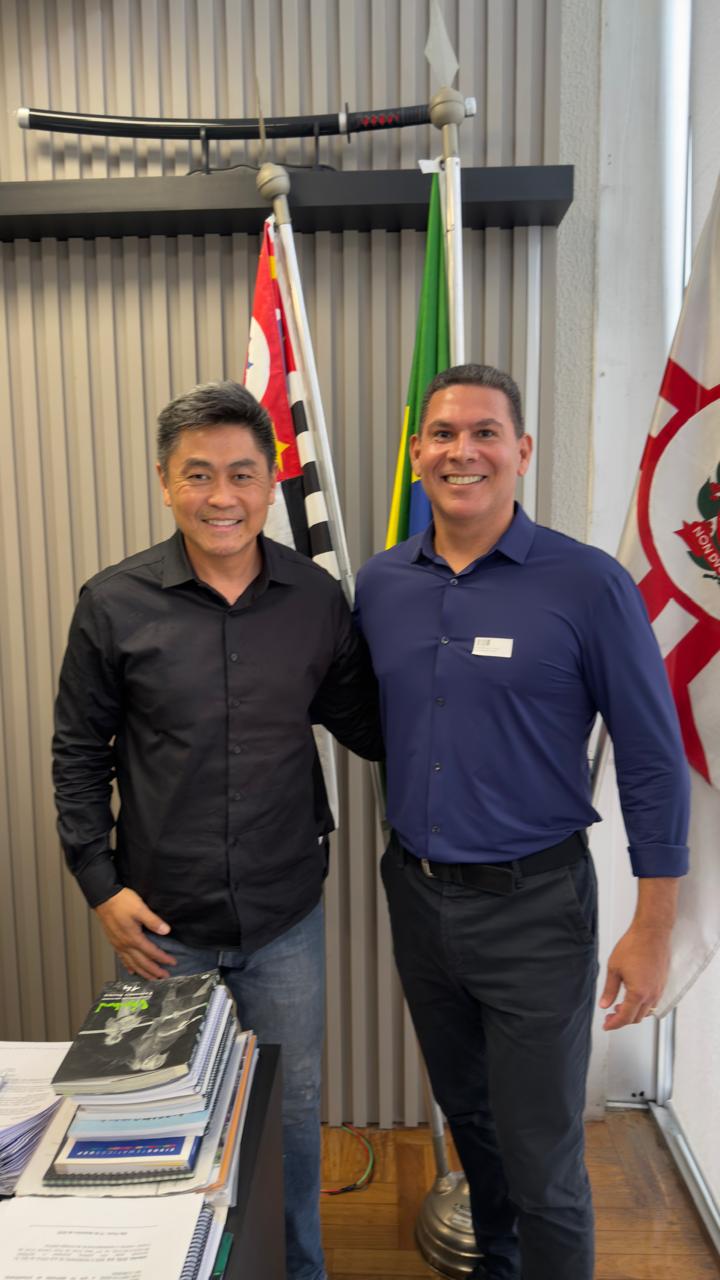 Eduardo Carlota ao lado do vereador de São Paulo Kenji Ito, em gabinete com as bandeiras de São Paulo, do Brasil e de Caraguatatuba.