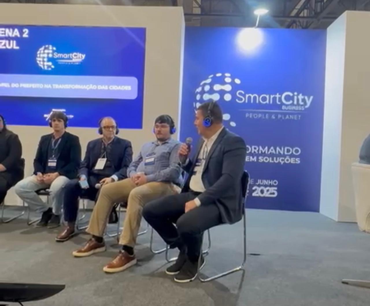 Eduardo Carlota participa de painel no Smart City Business, com microfone, ao lado de outros convidados.